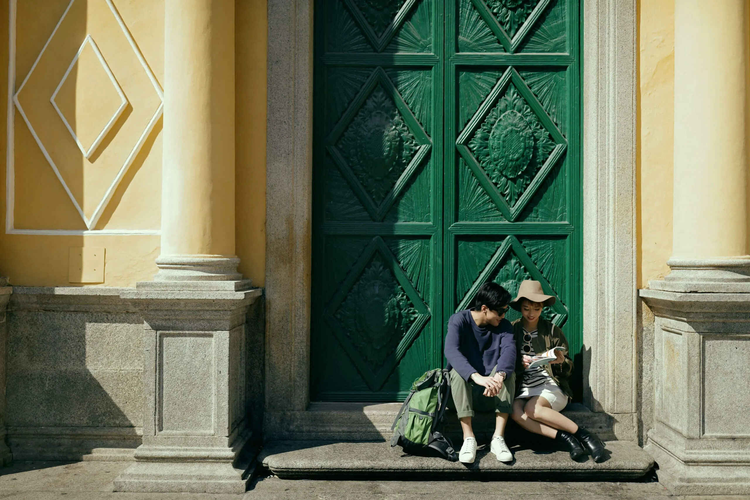 Two travellers sharing a guidebook on steps beside a green doorway in Macau